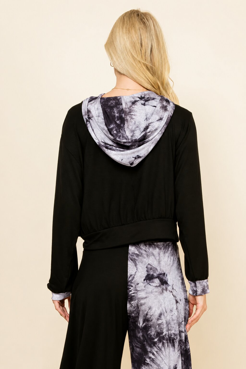 A woman shown from the back wearing a black long-sleeve top and matching pants with a gray and white tie-dye pattern on the hood lining, cuffs, and lower leg panels, against a plain beige background.
