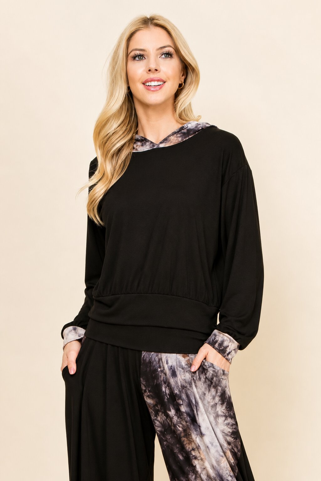 A woman modeling a black long-sleeve top with a gray and white tie-dye patterned collar, cuffs, and matching wide-leg pants, set against a solid beige background.