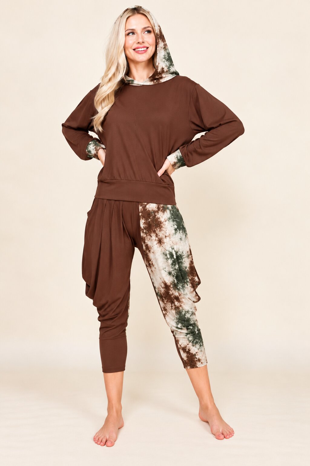 A woman modeling a two-piece lounge set featuring a brown long-sleeve top with a green and white patterned hood and matching patterned harem-style capri pants, posed against a solid beige studio background.