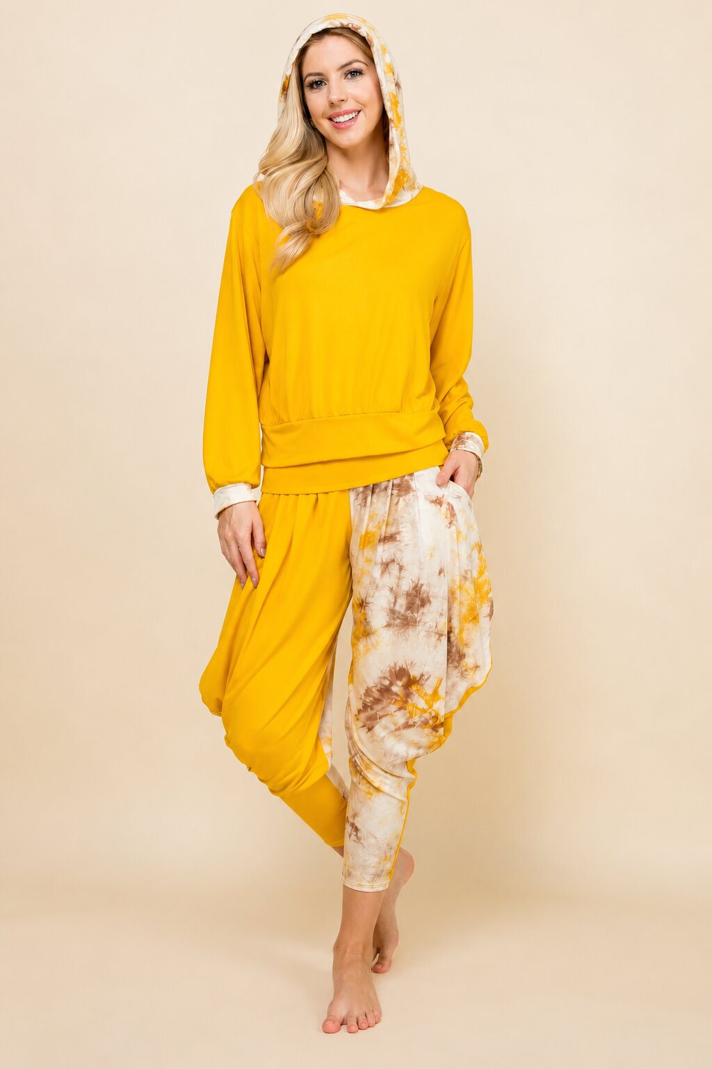 A woman modeling a two-piece lounge set consisting of a solid bright yellow sweatshirt and matching yellow harem pants, with the left leg of the pants featuring a white and yellow tie-dye pattern. She is also wearing a matching yellow patterned headscarf.