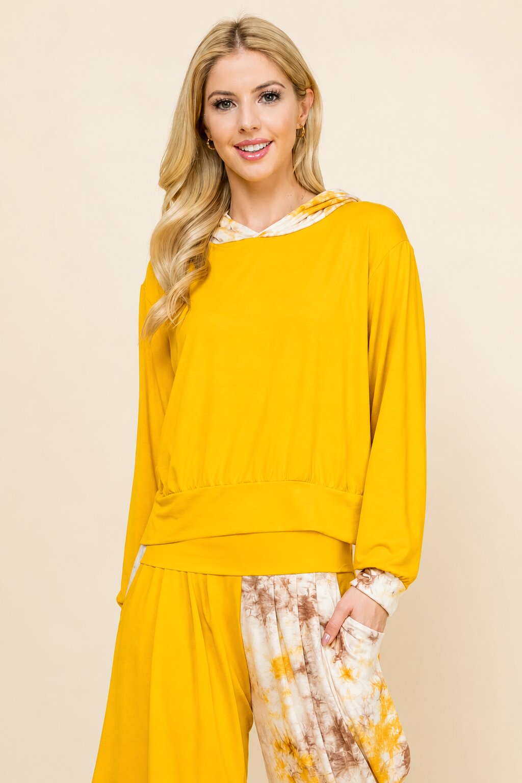 A woman modeling a bright yellow long-sleeve top with a white and yellow tie-dye patterned skirt, set against a plain beige studio background.