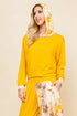 A woman modeling a bright yellow long-sleeve lounge set with a matching yellow and white tie-dye hooded sweatshirt and pants, set against a solid beige background.