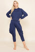 A woman modeling a navy blue two-piece loungewear set consisting of a long-sleeve cropped hoodie and matching draped capri pants, posed against a solid beige studio background.