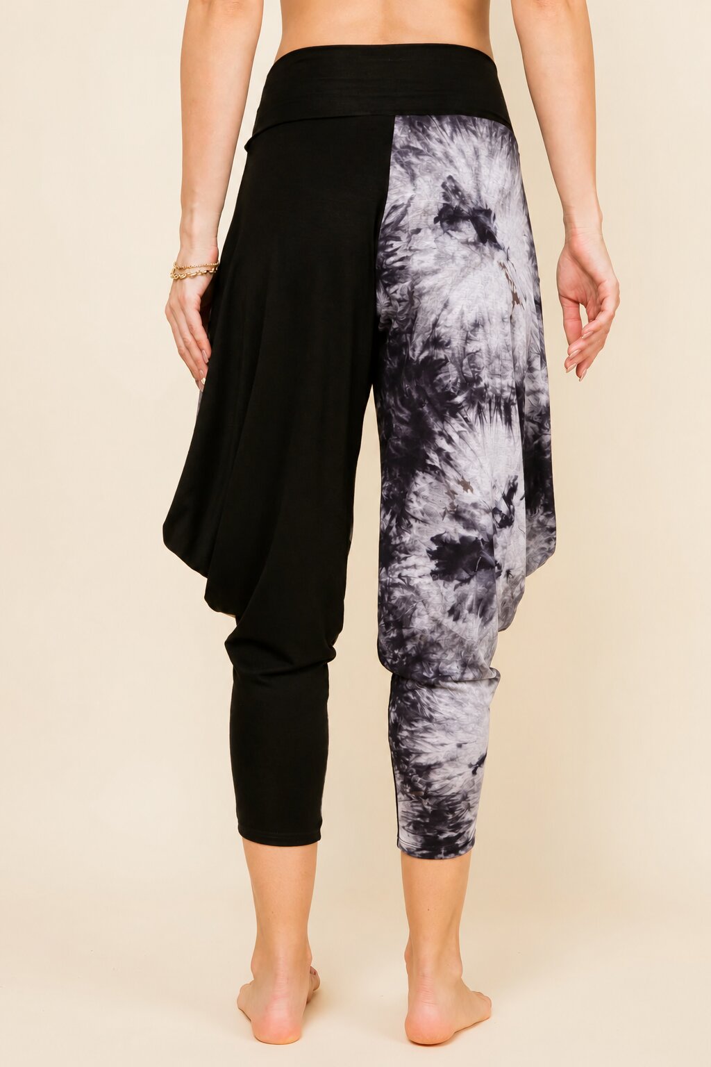 A person shown from the back wearing black harem-style cropped pants with a gray and white tie-dye pattern on one leg, against a plain beige studio background.
