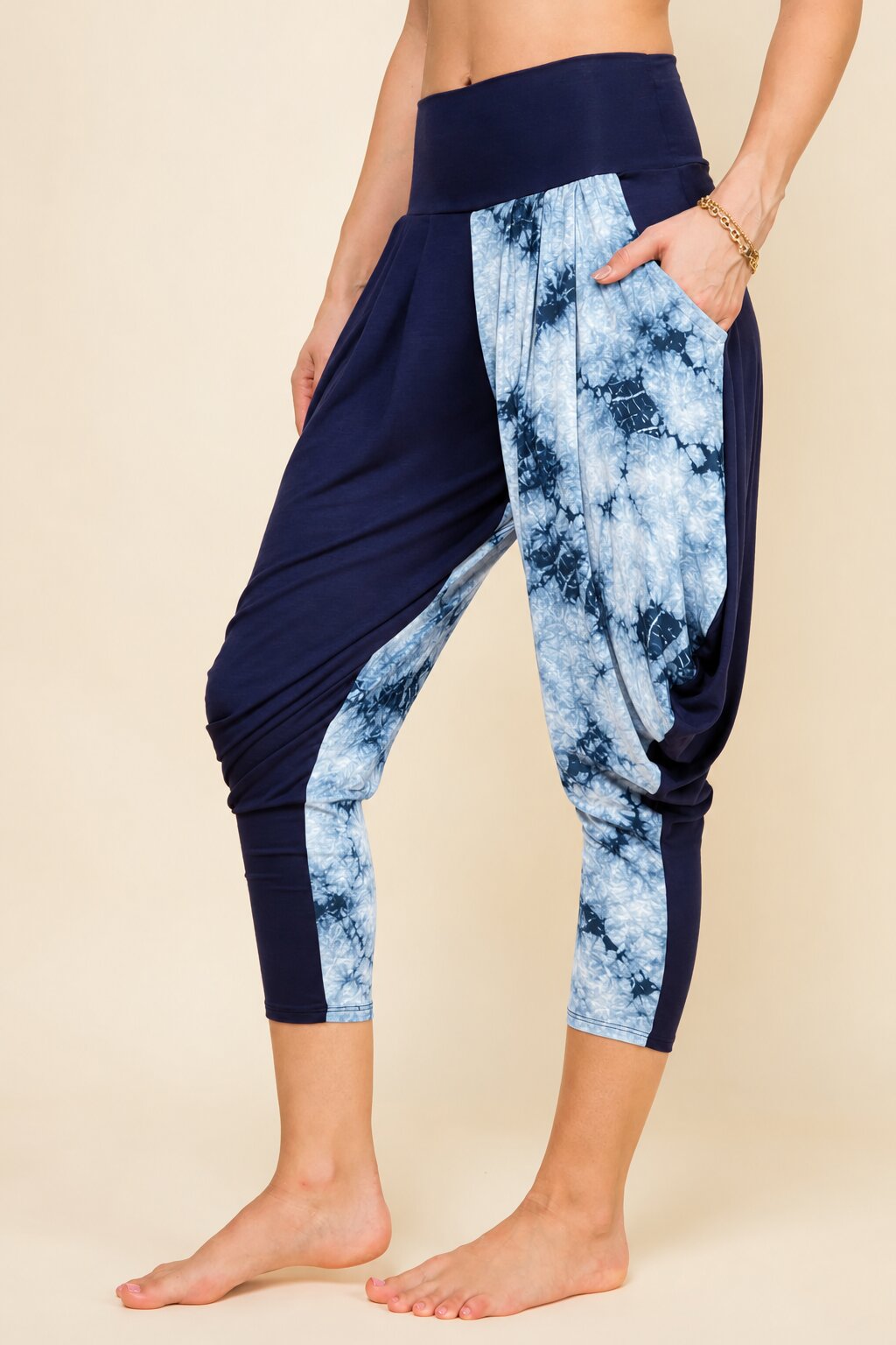 A model wearing high-waisted harem-style cropped leggings with navy blue and light blue tie-dye side panels, shown against a plain beige studio background.
